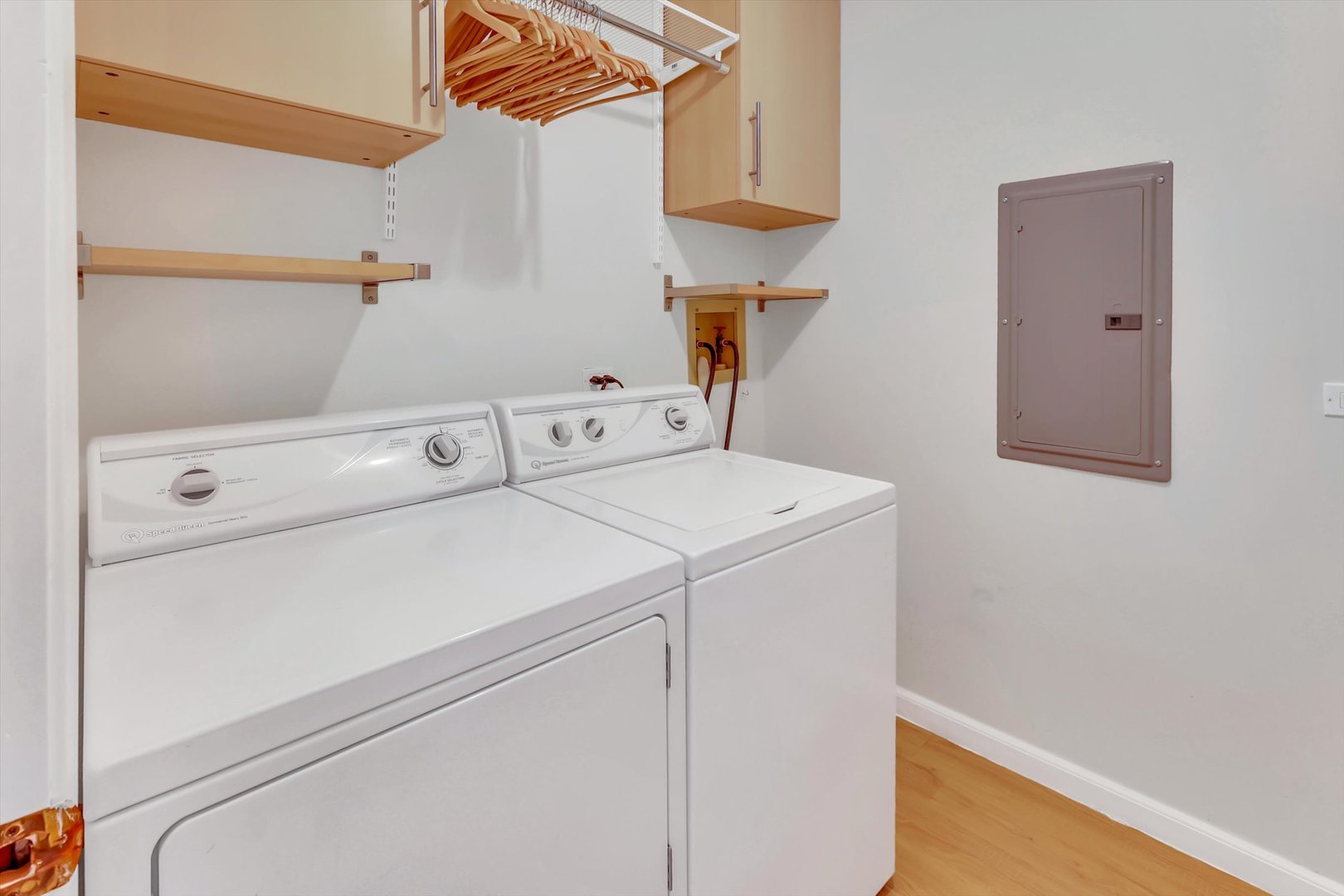 Laundry room with white washer and dryer beneath wooden shelves and hanging clothes hangers.