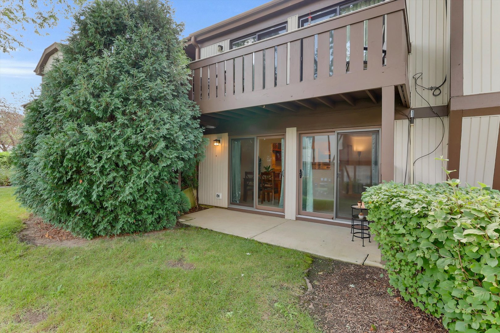 Rear exterior with a concrete patio, sliding glass doors, and elevated wooden balcony.