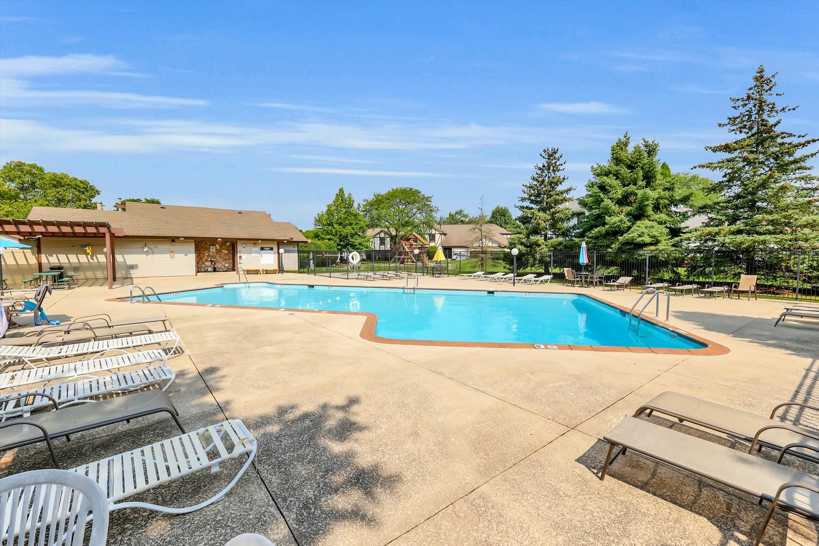Community swimming pool with lounge chairs, fenced deck, and a small pool building.