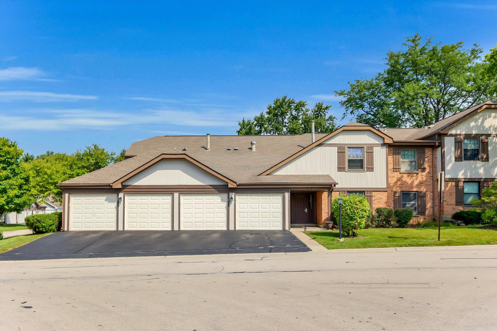 Multi-unit home with attached garage doors, beige siding, red brick, and a covered entry.