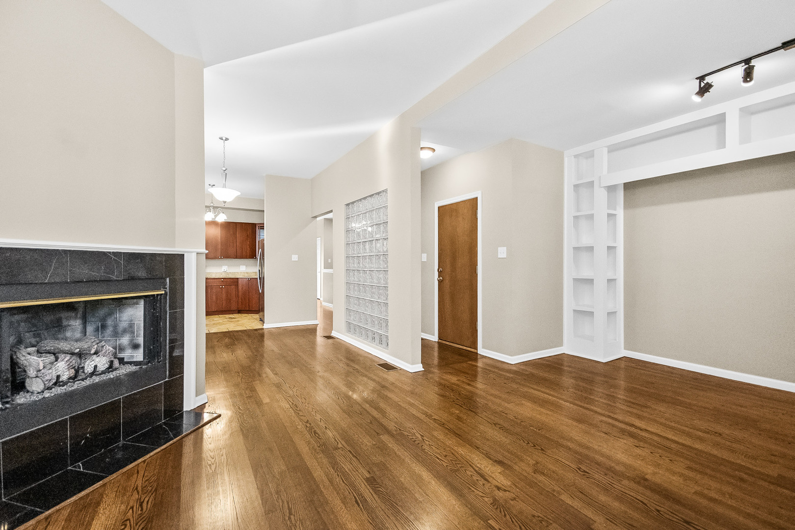 Living room with hardwood floors, black tiled fireplace, glass-block partition, and built-in shelving.