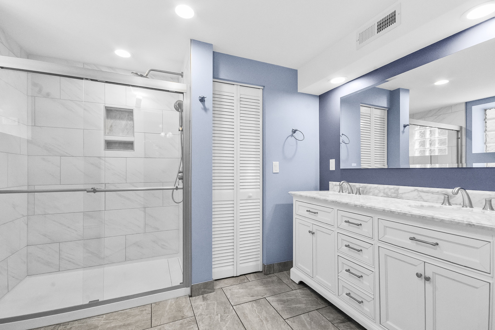 Bathroom with a glass-enclosed tiled shower and white double-sink vanity against blue walls.