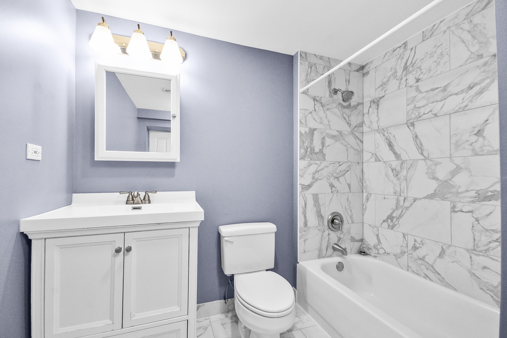 Bathroom with a white vanity, toilet, and bathtub surrounded by marble-look tile.