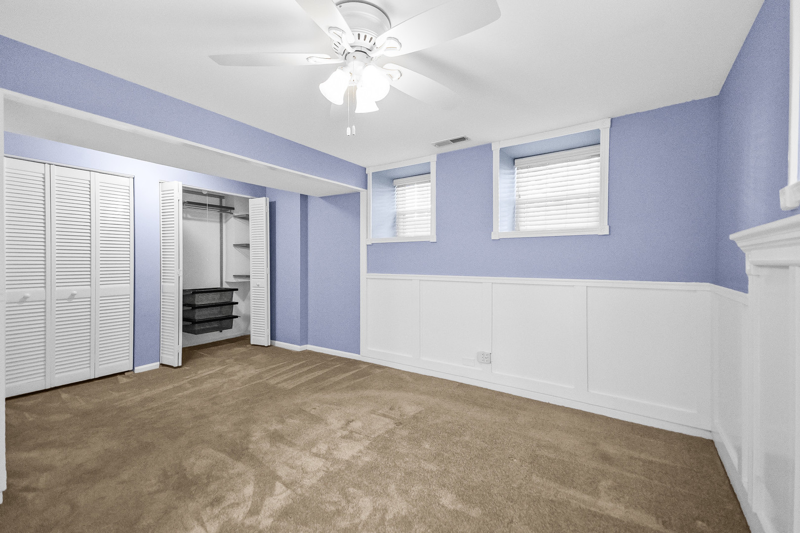 Vacant bedroom with lavender walls, carpet, louvered closets, and ceiling fan.