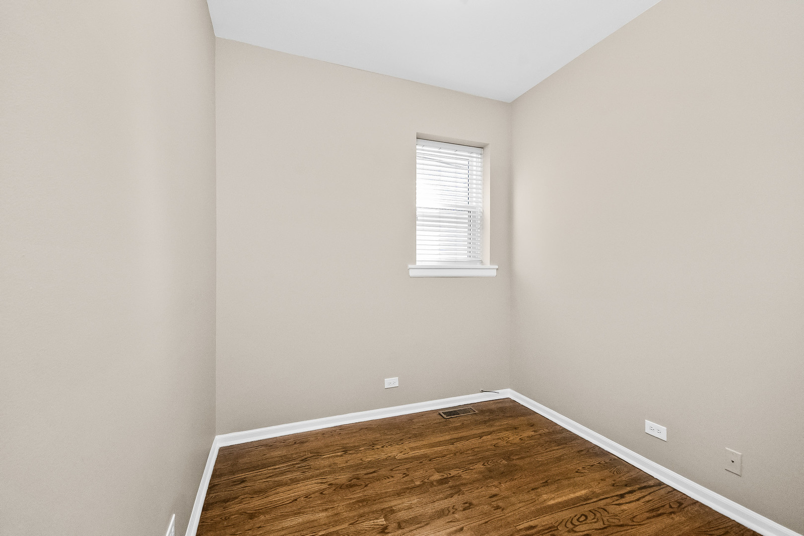 Empty room with dark hardwood floors and a small window with white blinds.
