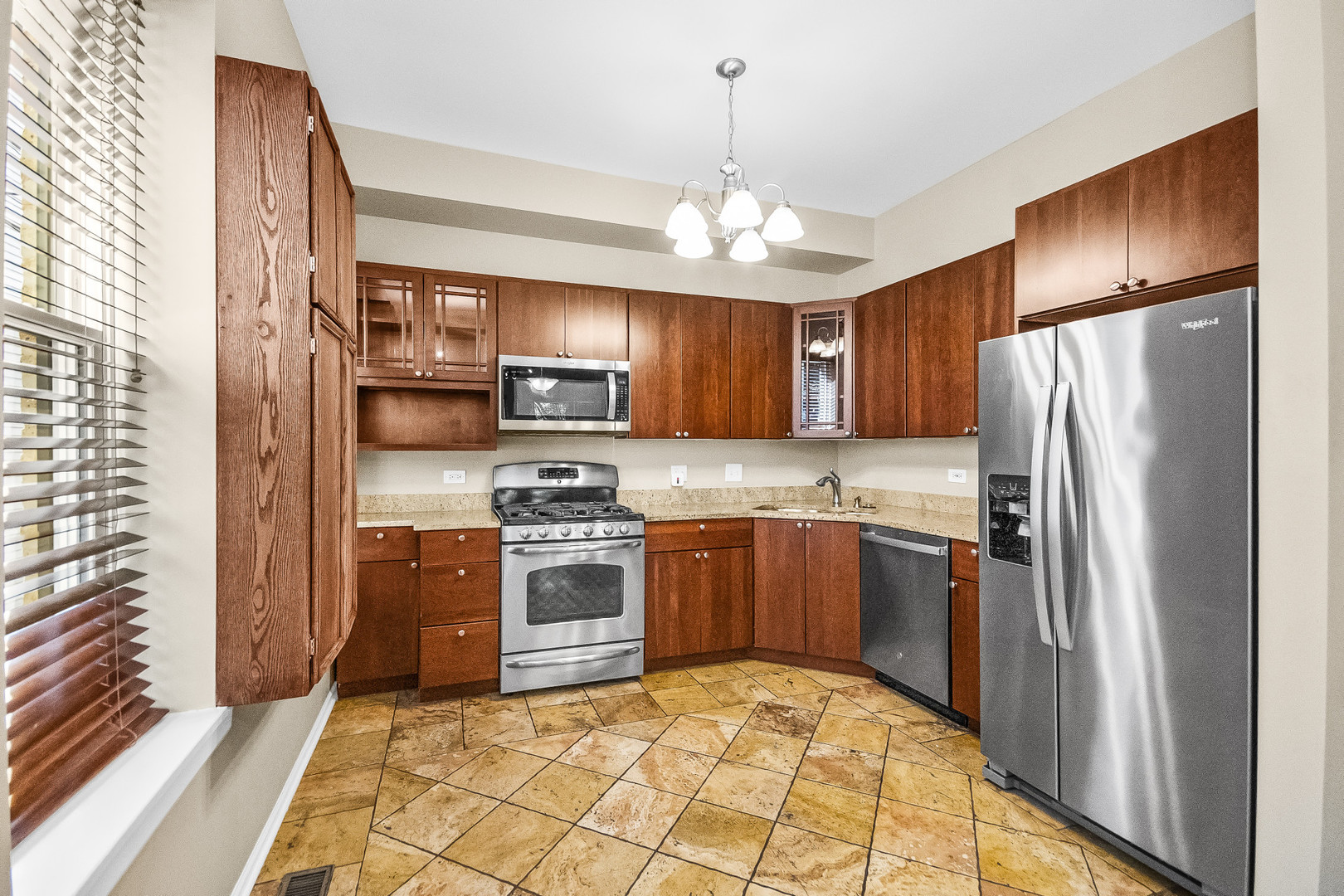 Kitchen with dark wood cabinets, stainless steel appliances, and tan tile flooring.