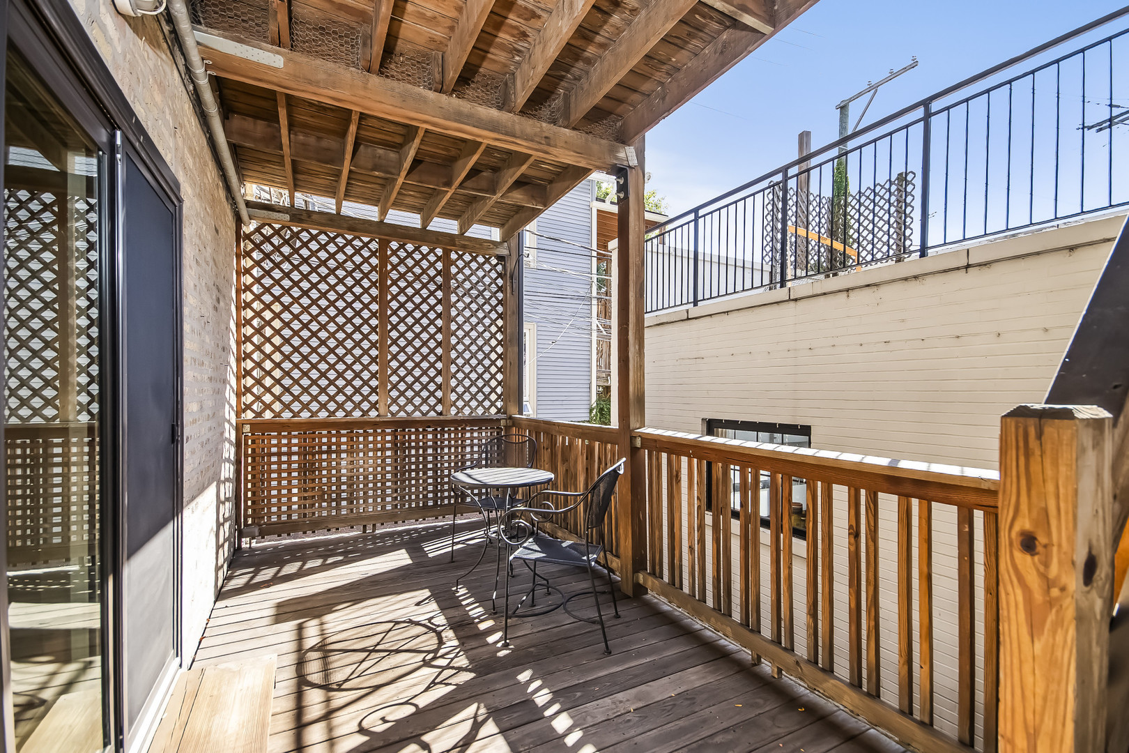 Covered wooden deck with lattice screens and a small table and chairs.