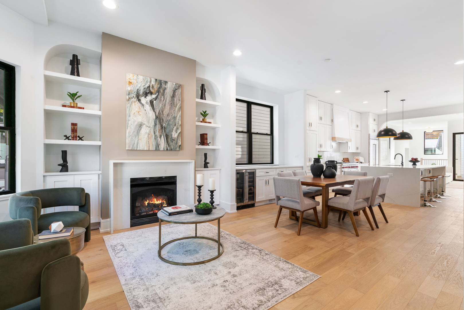 Open-plan living and dining room with a lit fireplace, built-in shelves, and kitchen island.