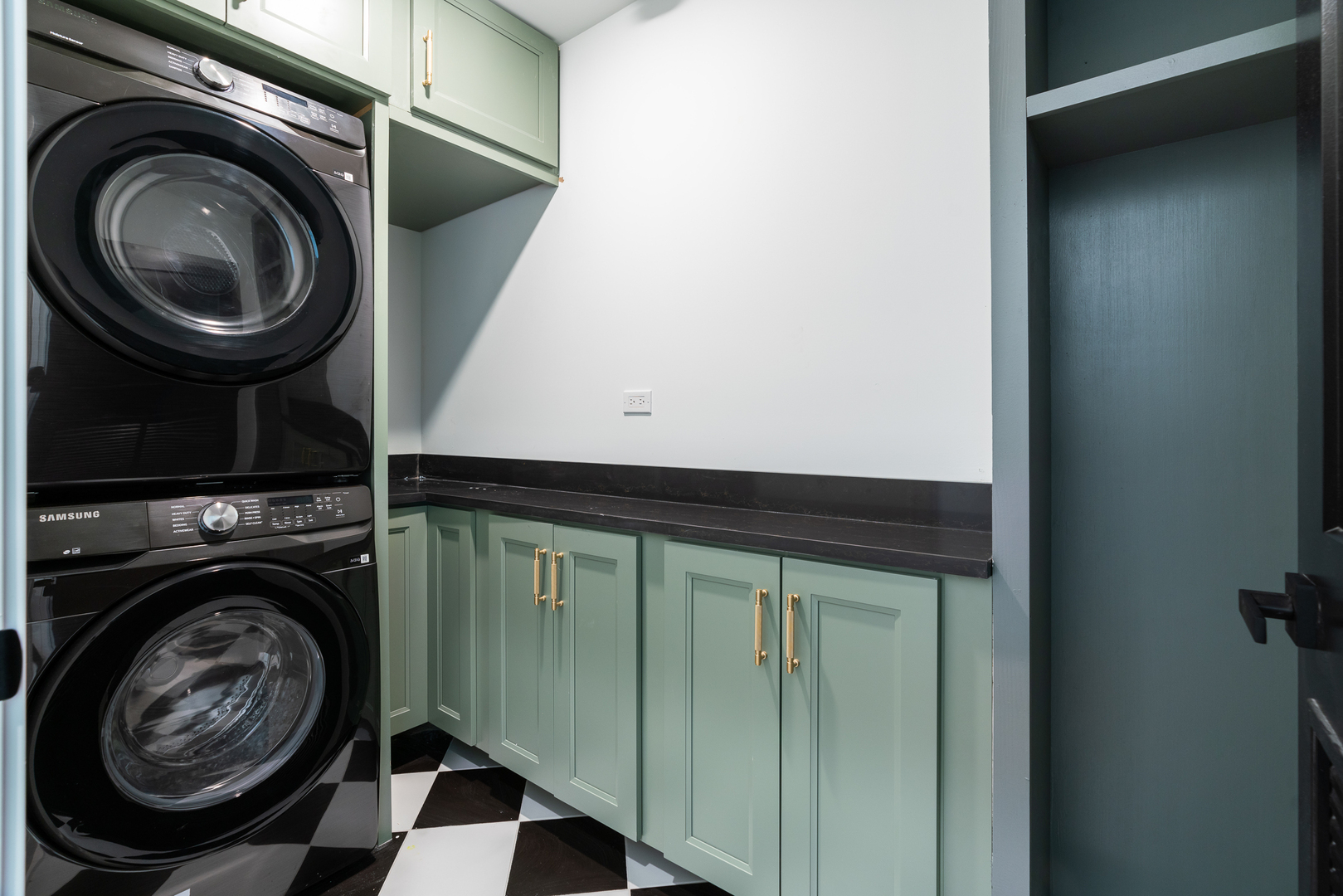 Laundry room with stacked washer and dryer, sage-green cabinetry, and checkerboard flooring.