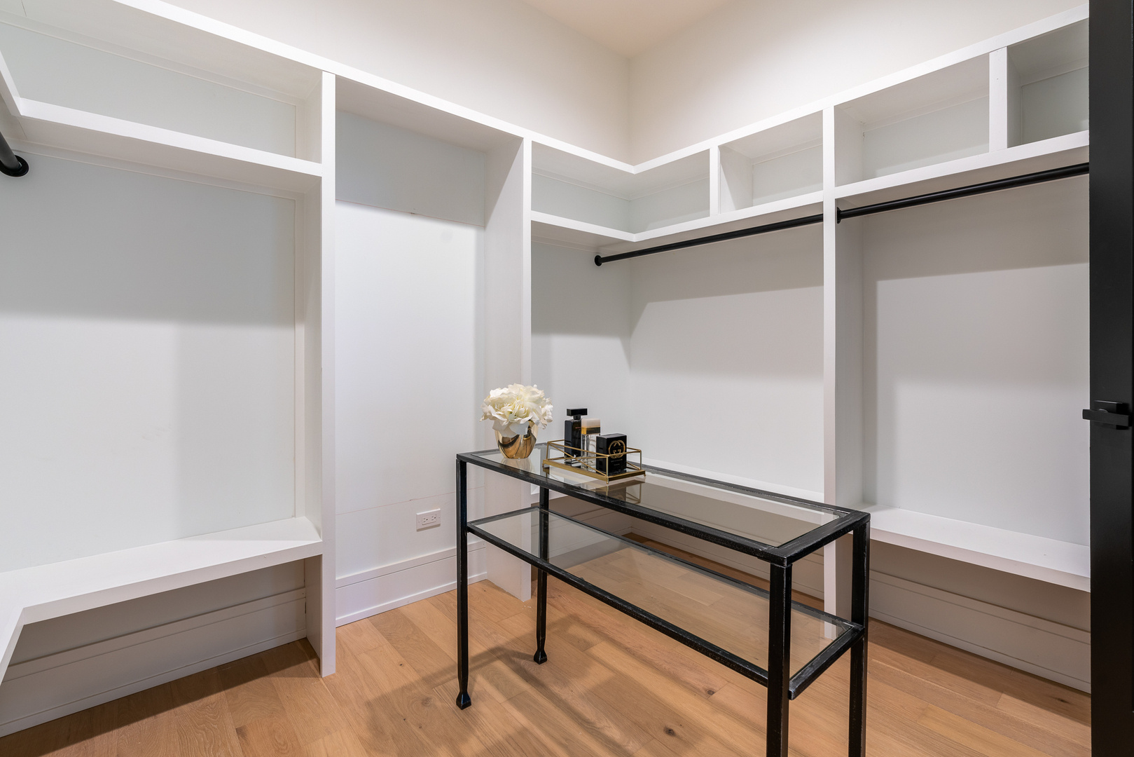 Walk-in closet with white built-in shelving, black hanging rods, and a glass-top console table.