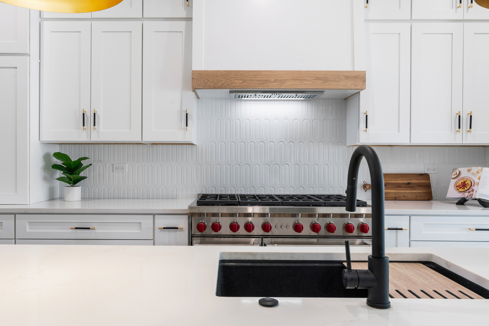 White kitchen with a stainless gas range, patterned tile backsplash, and black sink faucet.