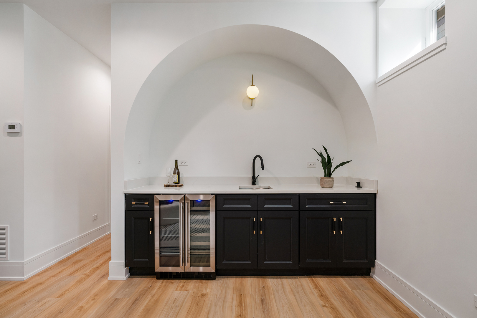 Wet bar with black cabinetry, twin glass-front beverage refrigerators, and a large arched wall niche.