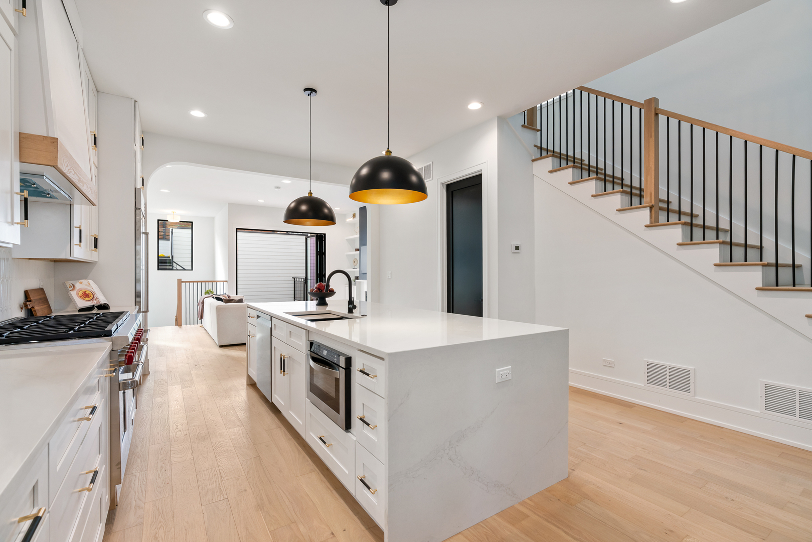 Open-plan kitchen with a large white island, black pendant lights, and a staircase with black railings.