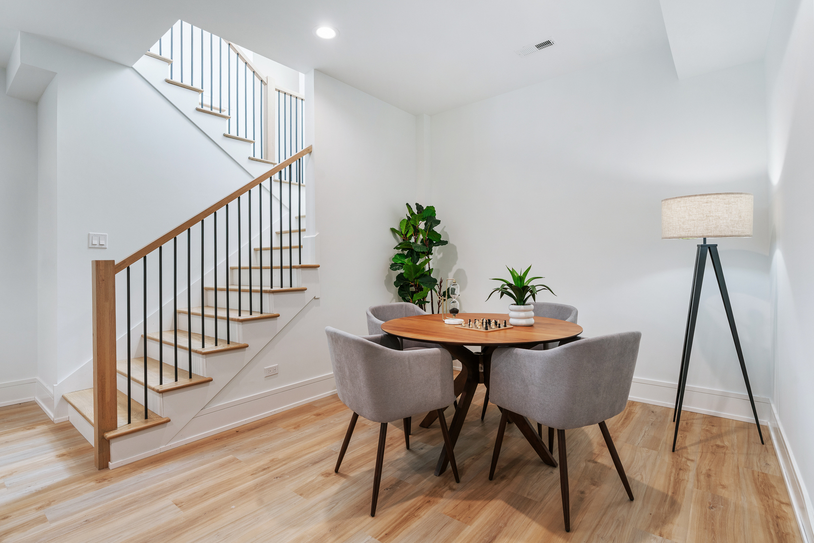 Dining area with a round wood table beside an open staircase with wood treads and black railings.