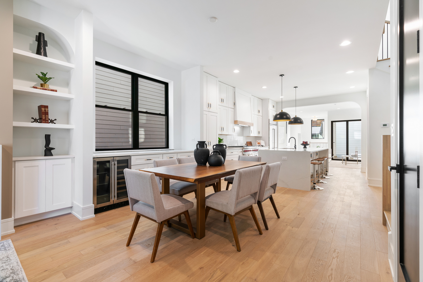 Open kitchen and dining area with a large island, black-framed windows, and a wood dining table.