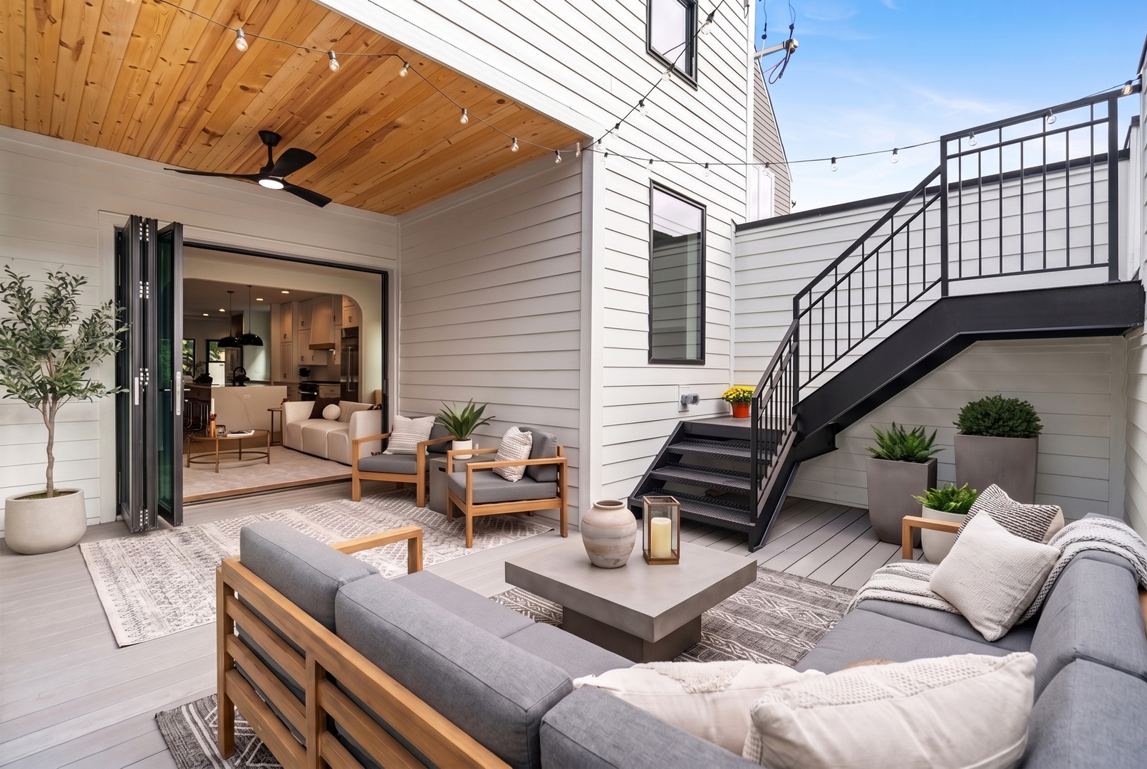 Rooftop terrace with lounge seating, a wood-plank ceiling, and black metal stairs beside open folding doors.