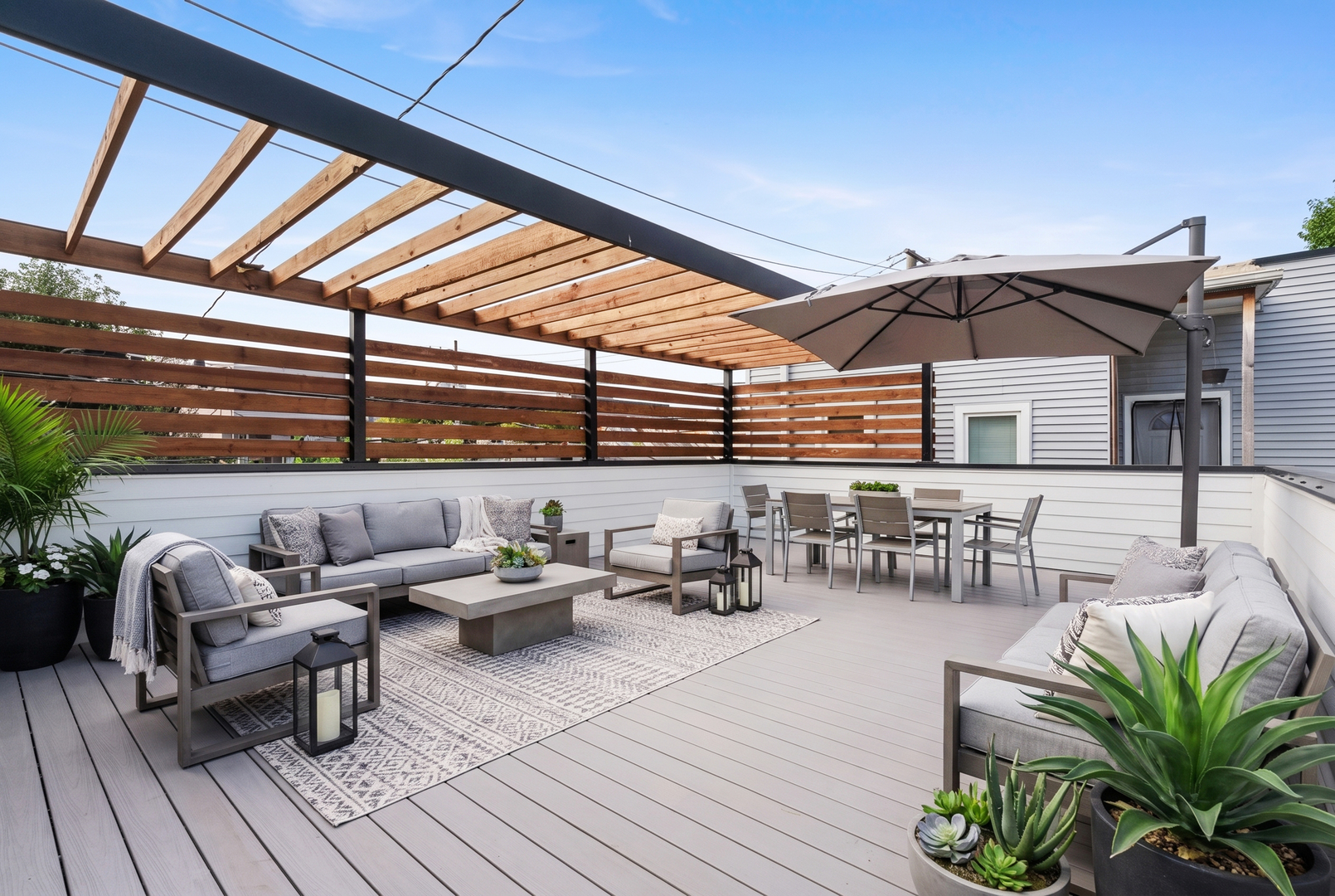 Furnished outdoor deck with a wood pergola, lounge seating, dining set, and potted plants.