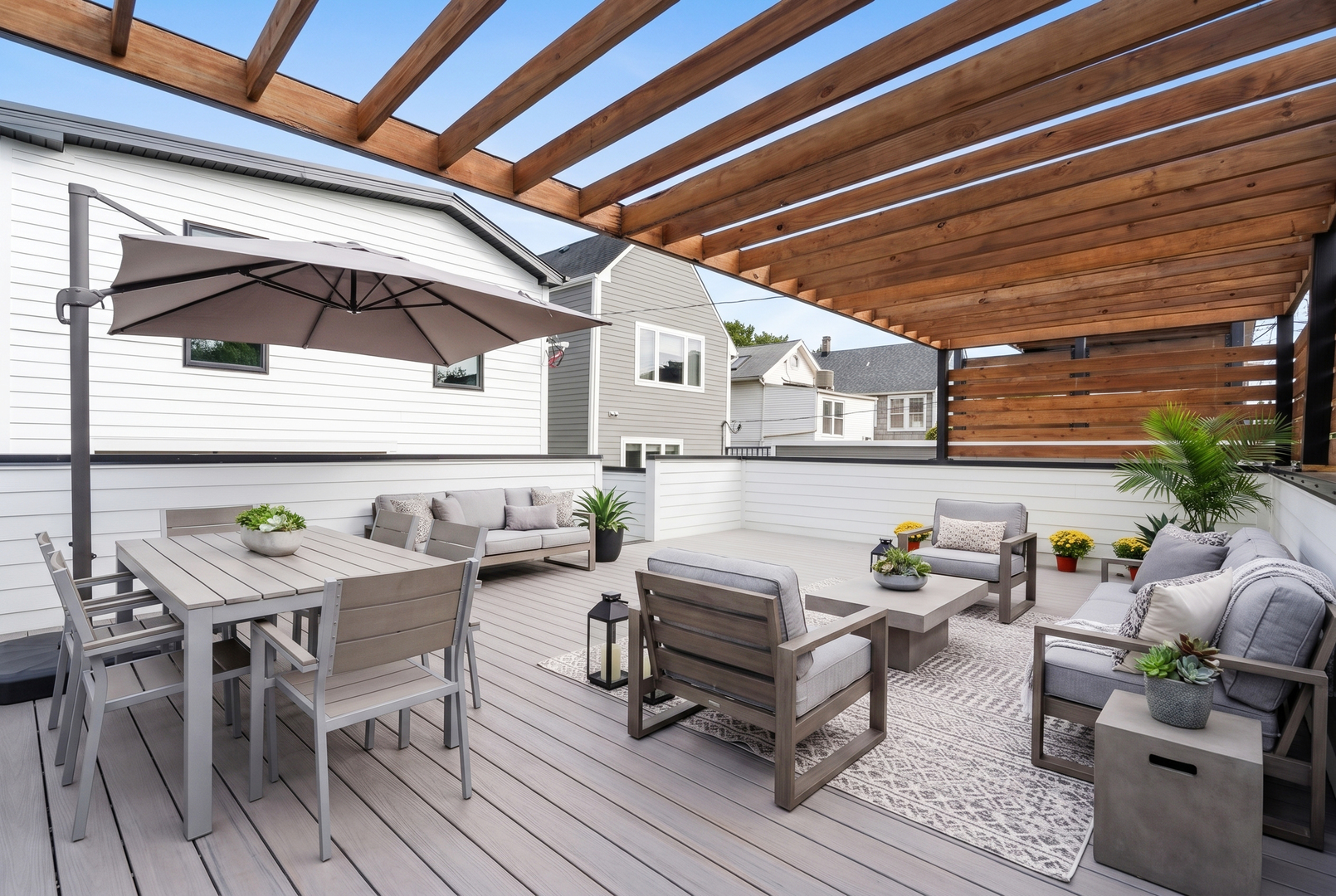 Furnished rooftop deck with timber pergola, lounge seating, dining table, and potted plants.