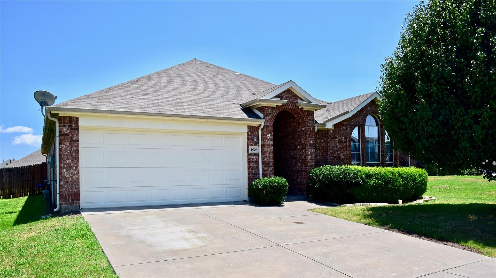 Red brick house with a wide white garage, arched entry, and landscaped lawn.