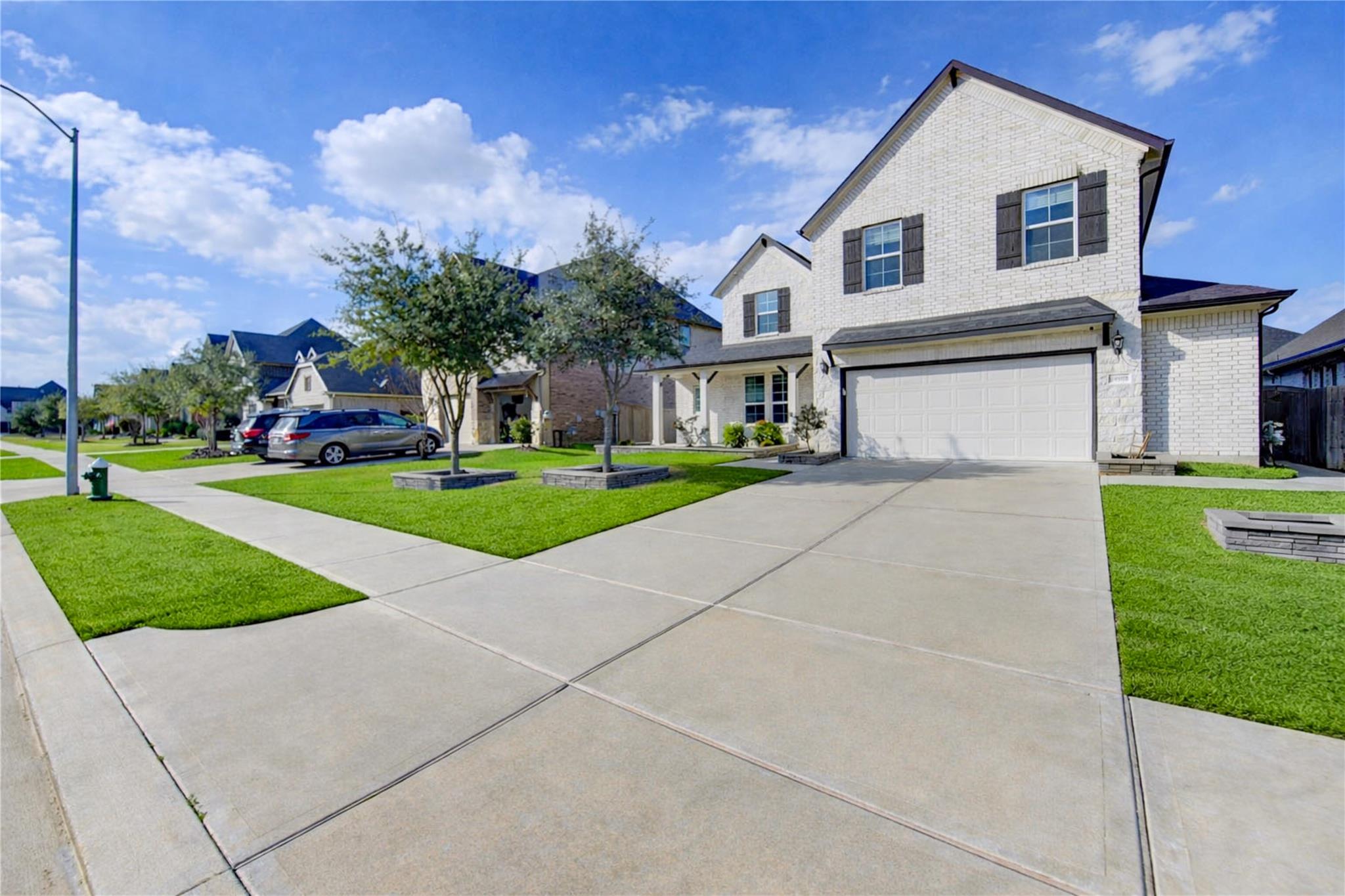Two-story white brick home with dark shutters, double garage, and a wide driveway.