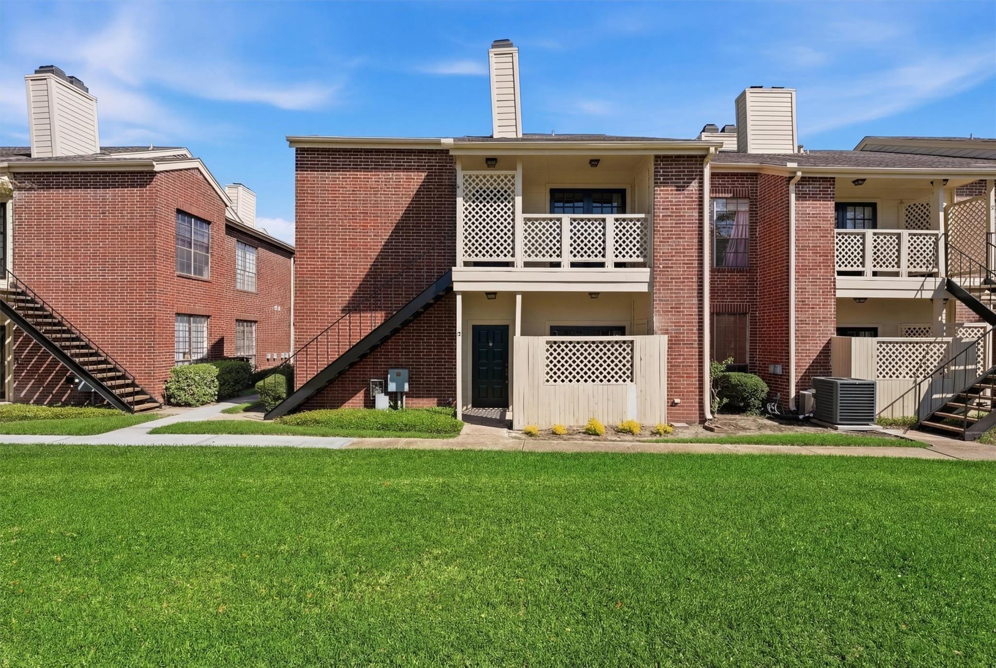 Brick apartment building with lattice balconies and exterior stairs behind a broad green lawn.