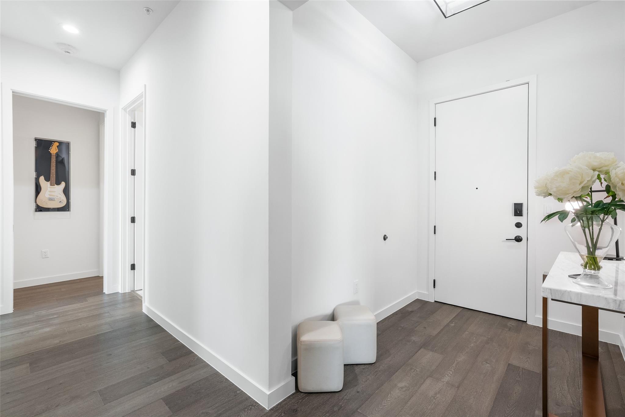 Apartment entry foyer with a white front door, gray flooring, and a flower-topped console.
