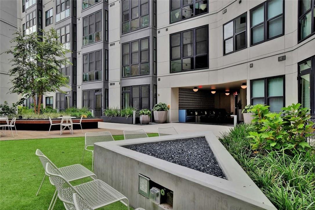 Apartment courtyard with a green lawn, white patio chairs, planters, and a covered entrance.