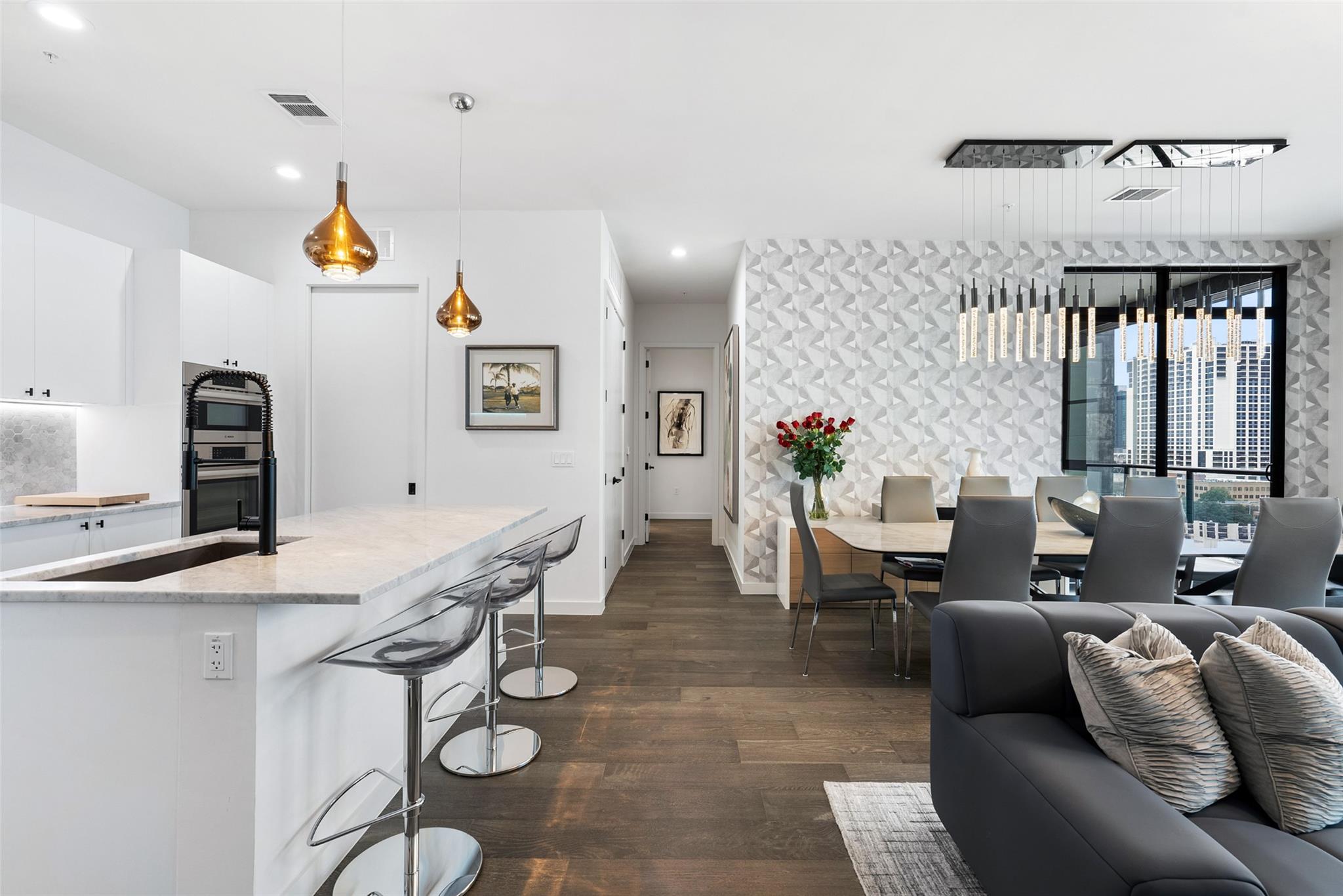Open-plan condo kitchen and dining area with a white island, geometric wallpaper, and downtown views.