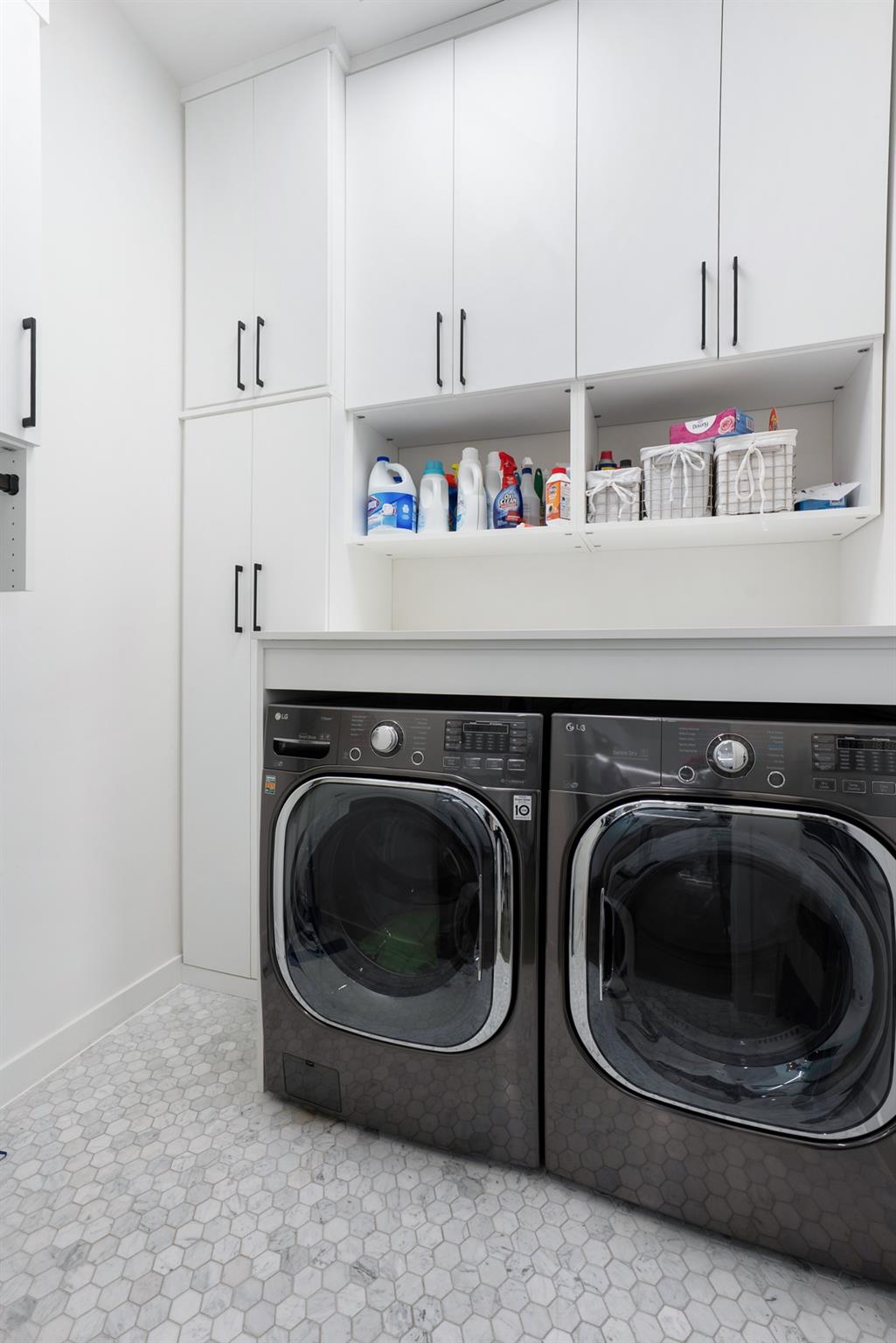 Laundry room with side-by-side front-loading washer and dryer beneath white cabinets.