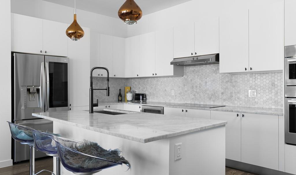 Modern white kitchen with a large island, hexagonal tile backsplash, and copper pendant lights.