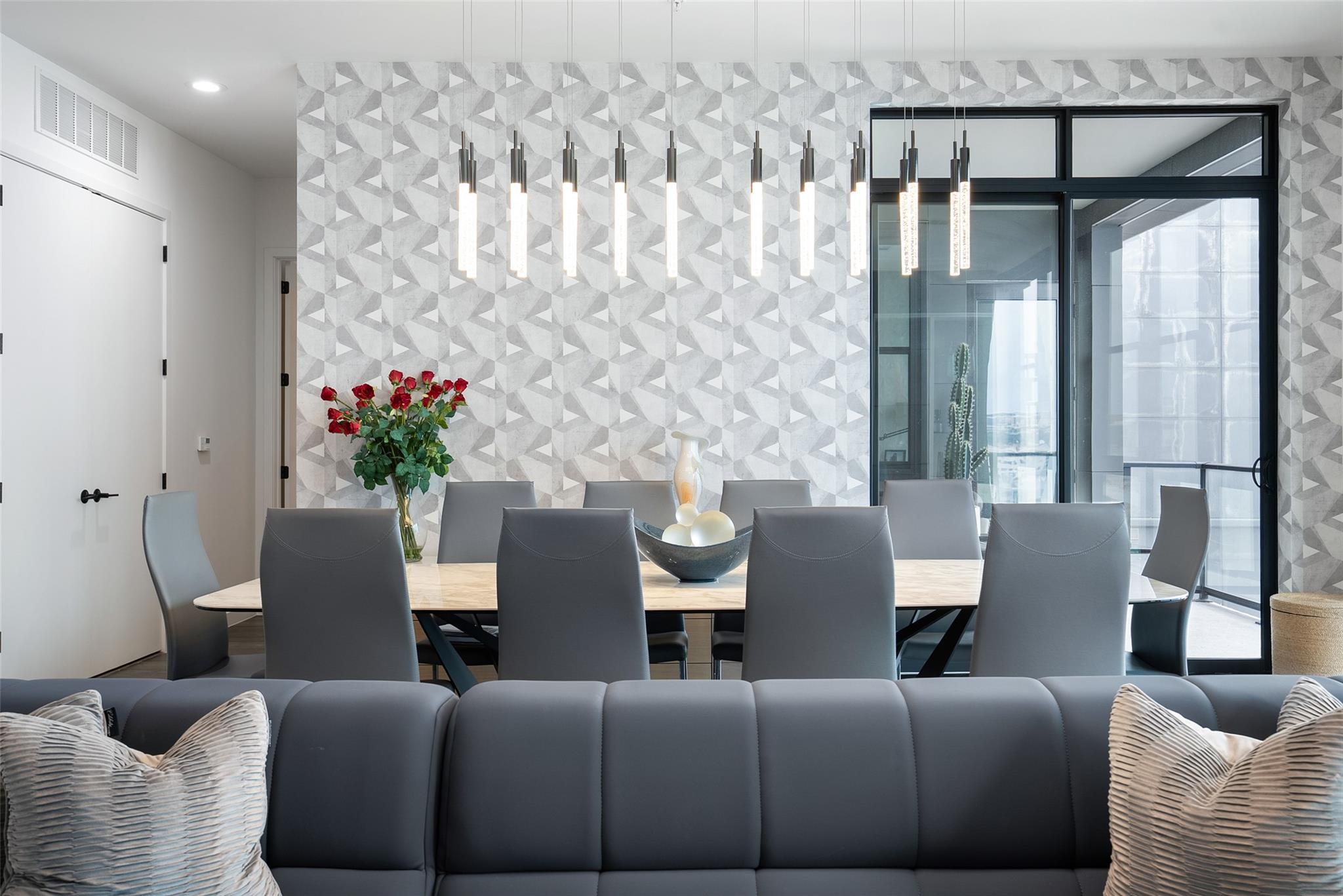 Dining area with geometric wallpaper, pendant lights, and a table beside large glass doors.