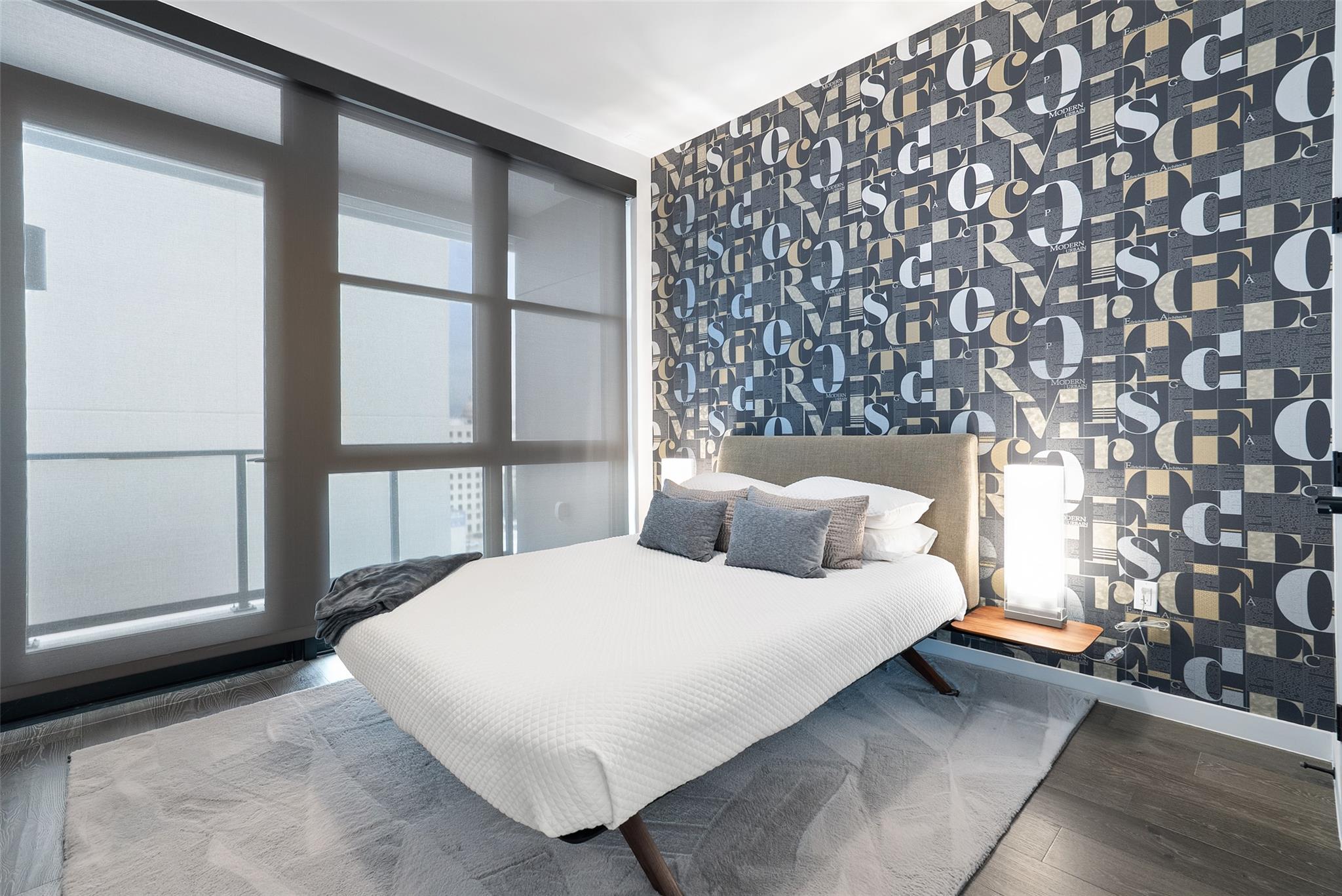 Modern condo bedroom with a white bed, floor-to-ceiling windows, and bold typographic wallpaper.