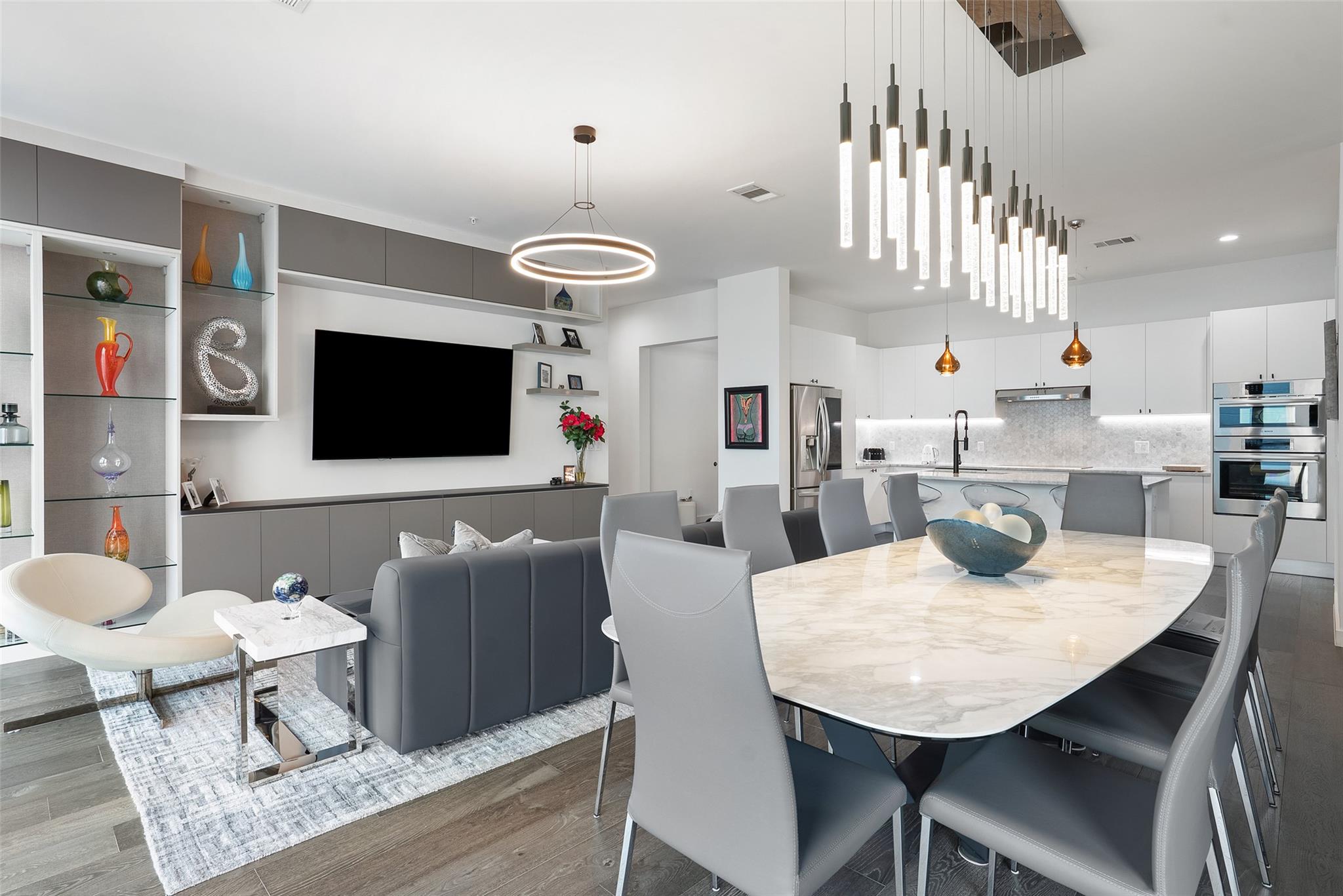 Open-plan living and dining area with a marble table and dramatic pendant lighting beside a modern kitchen.
