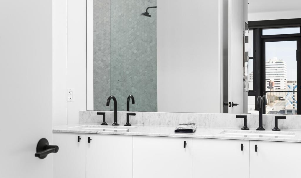 Modern bathroom with a marble double vanity, black faucets, and a city view through the window.