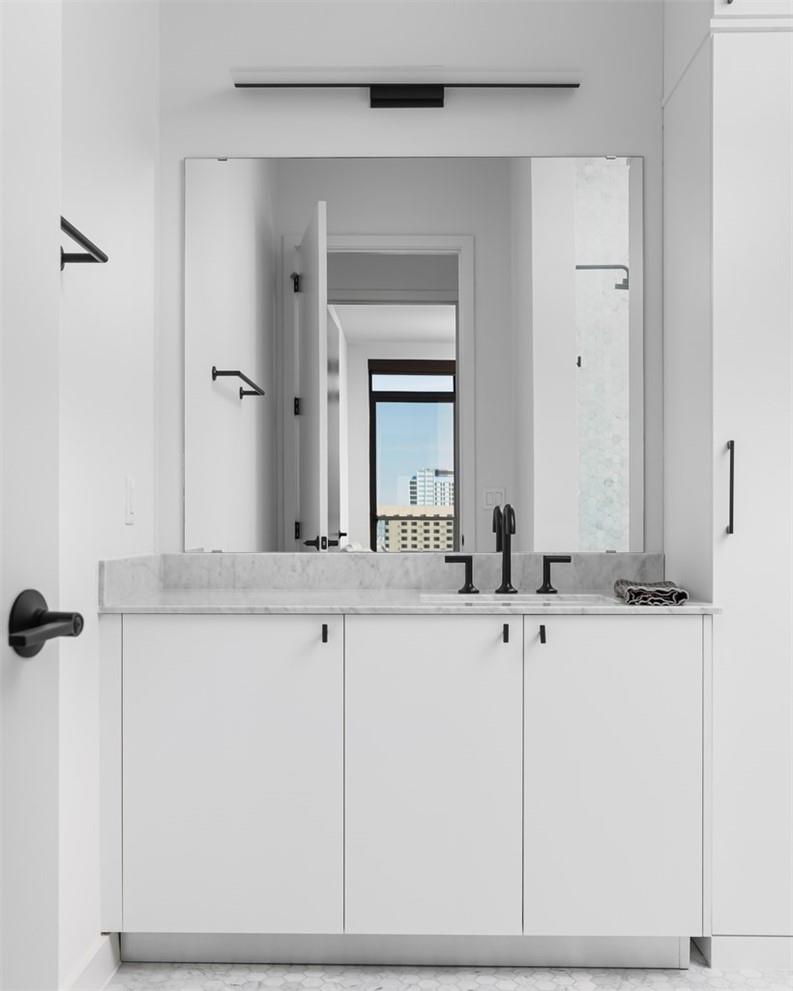 Bathroom with a white double vanity, marble counter, large mirror, and black fixtures.