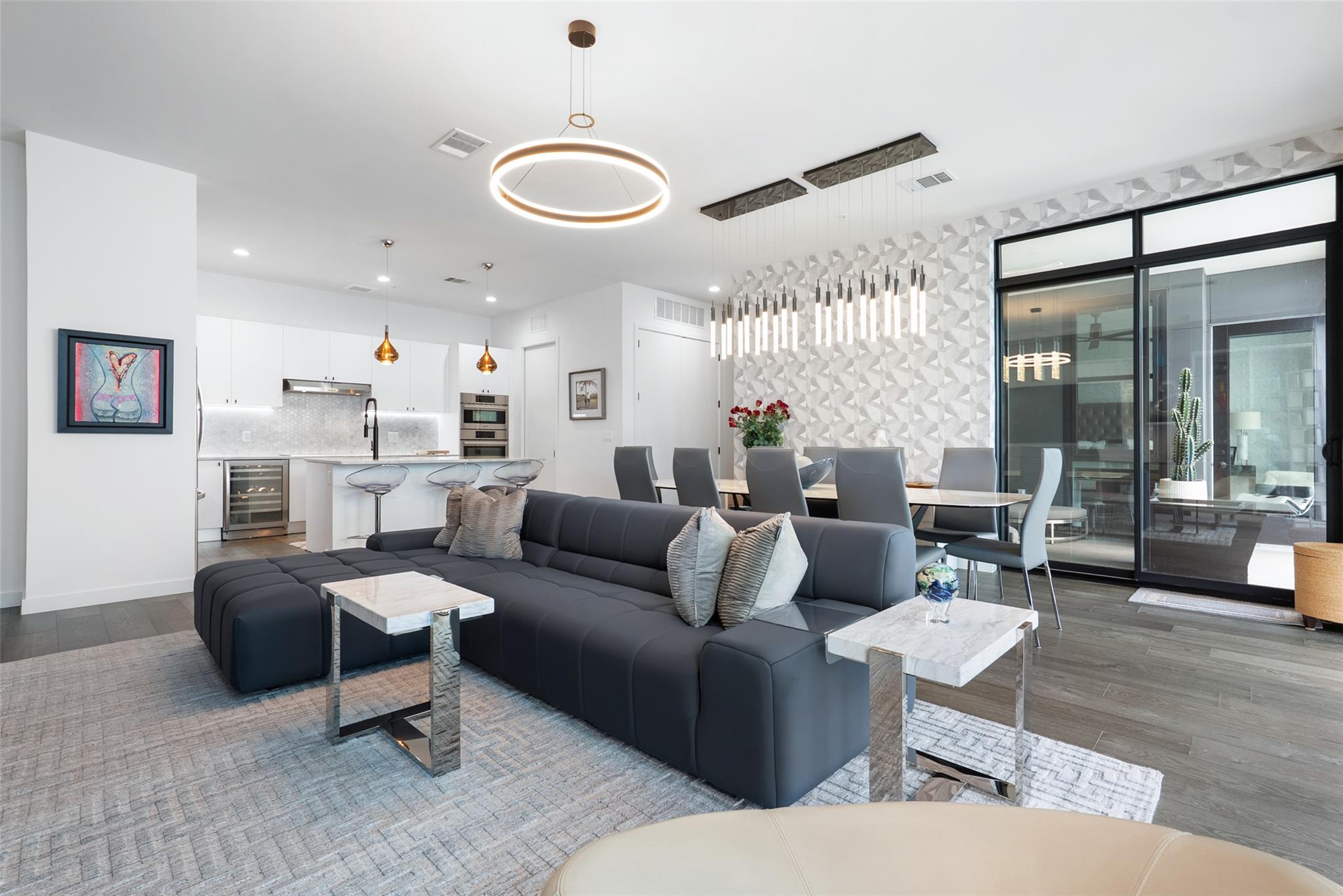 Open-plan condo living room with a charcoal sectional, geometric accent wall, and adjoining modern kitchen.