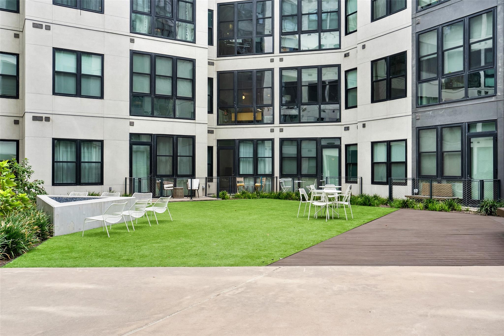 Apartment courtyard with a green lawn, white outdoor seating, and a wooden deck.