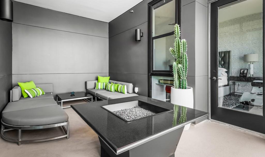 Apartment terrace with gray lounge seating, green cushions, a cactus, and a rectangular fire pit table.