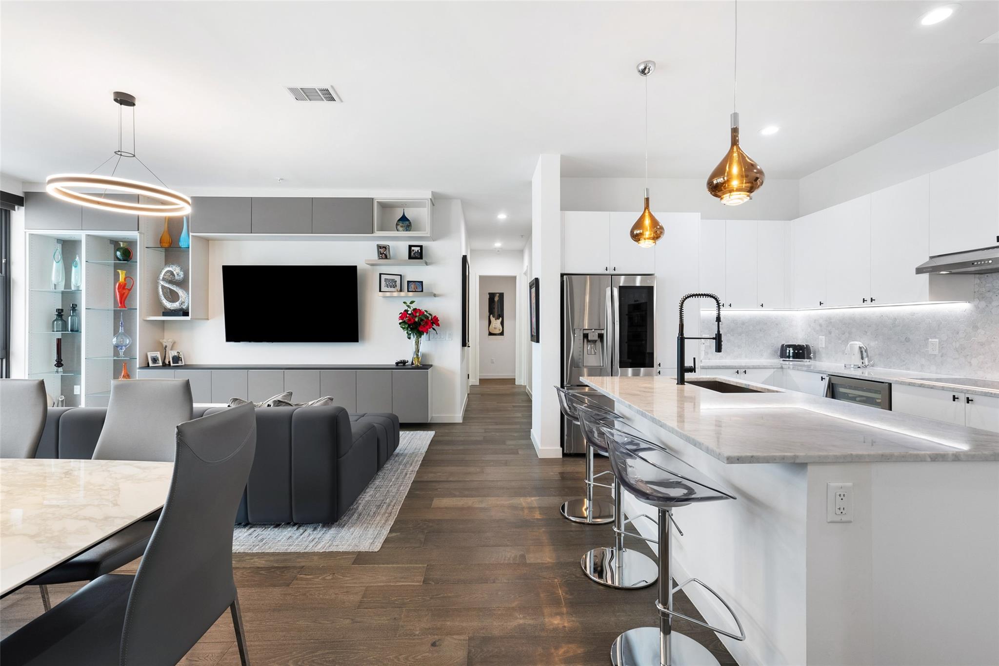 Open-plan condo kitchen and living area with a large marble island, white cabinetry, and dark wood floors.