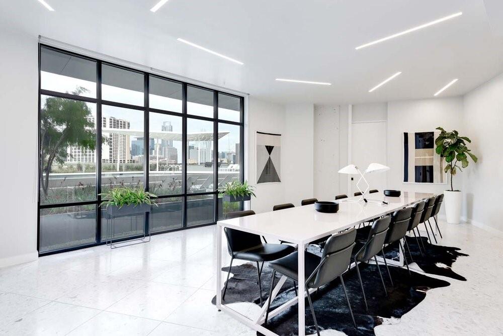 Furnished meeting room with a long conference table and floor-to-ceiling windows overlooking a city skyline.