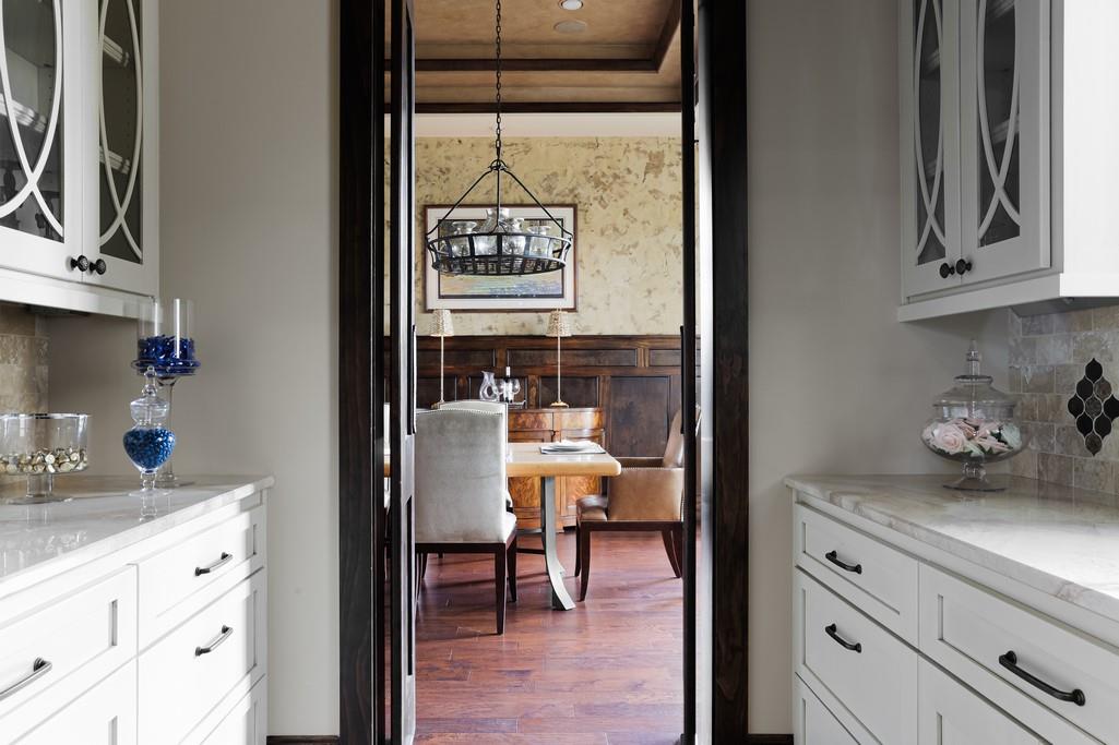 Kitchen with white cabinets and stone counters opening onto a dining room with a chandelier.