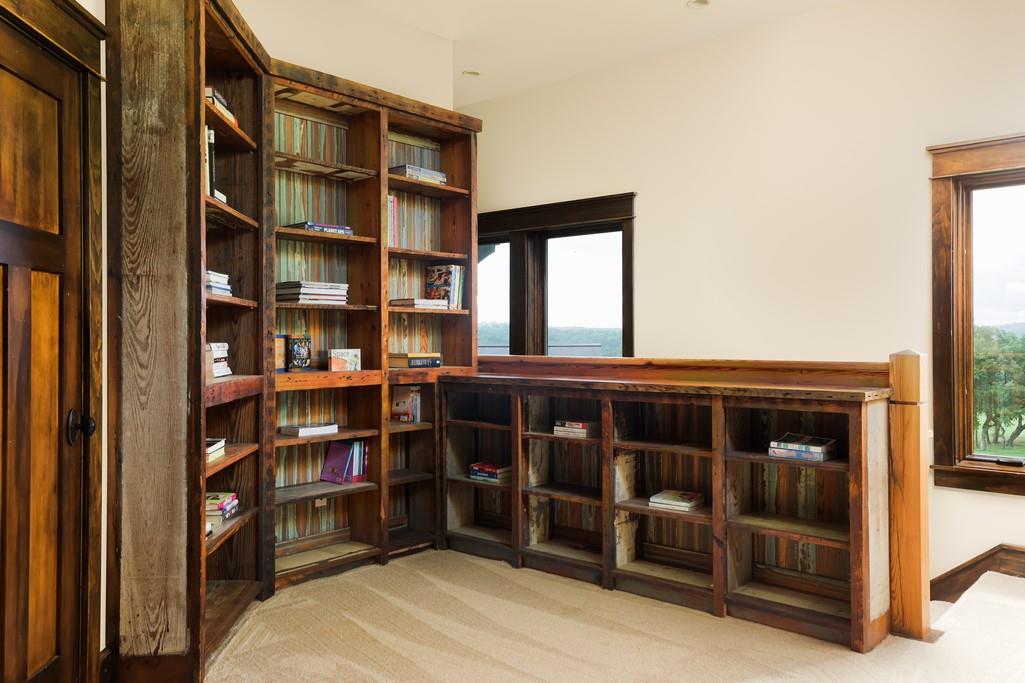 Home library with floor-to-ceiling wooden bookshelves and windows overlooking greenery.