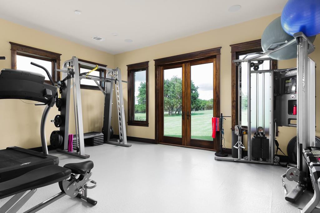 Home gym with treadmills and strength-training equipment beside glass doors overlooking a lawn.
