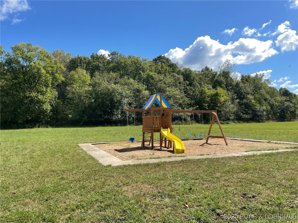 Playground with a wooden playset, yellow slide, and swings on a grassy lawn backed by trees.