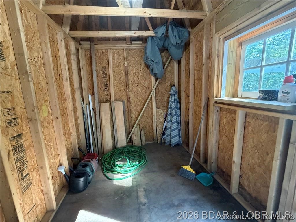 Unfinished storage room with exposed wood framing, a large window, and a coiled green garden hose.