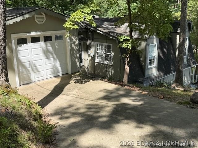 Gray home with a white garage and concrete driveway beneath leafy trees.