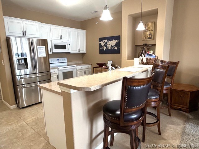 Kitchen with white cabinets, stainless steel appliances, and a large breakfast bar lined with dark wooden stools.