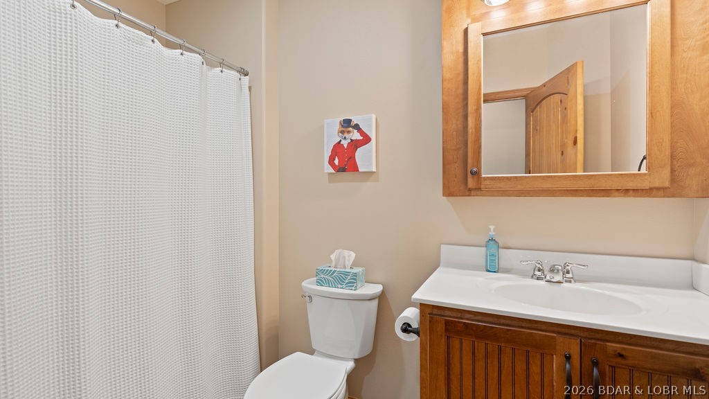 Bathroom with a white shower curtain, toilet, and wood vanity with a mirrored cabinet.