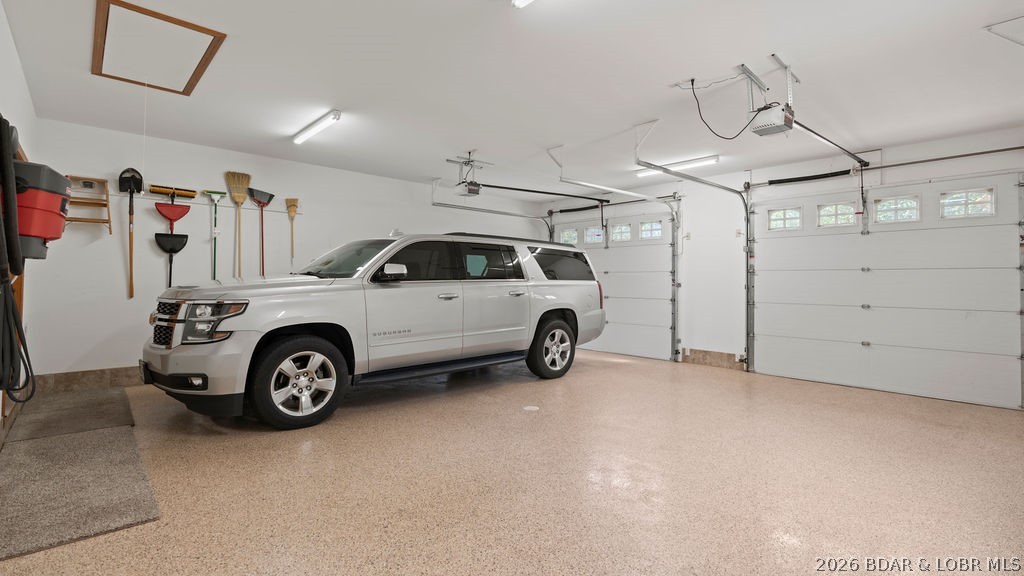 Spacious garage with a white SUV, speckled floor, wall-mounted tools, and two overhead doors.