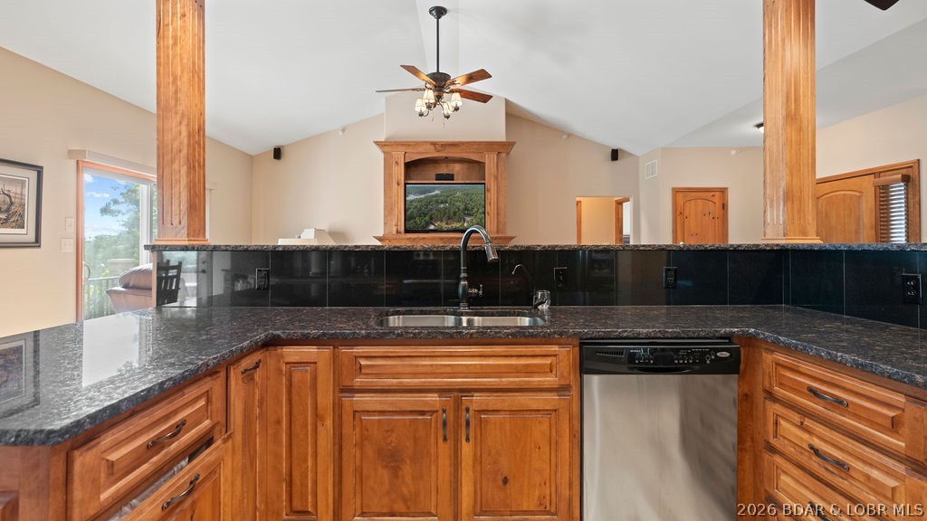 Kitchen with honey-toned wood cabinets, dark granite counters, black backsplash, and stainless-steel dishwasher.